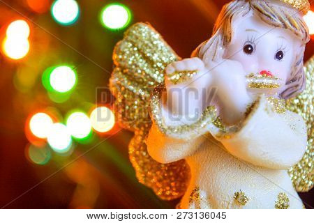 Figurine Of Little Angel With Golden Shiny Wings And Halo That Plays Flute On Shining Background Of 