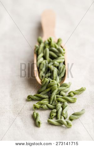 Uncooked spinach gemelli pasta in scoop.