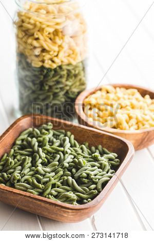 Uncooked spinach gemelli pasta in wooden bowl.