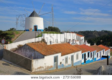 A Row Of Colorful Houses Along A Steep Cobbled Street Inside Odeceixe (near Aljezur), With A Whitewa