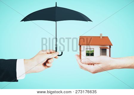 Hands Holding House And Umbrella On Sky Background. Real Estate And Assuarance Concept