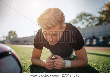 Young Blonde Player Stand In Plank Position On Football Lawn. He Is Concentrated. Ball Lying Besides