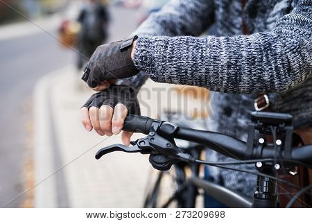 A Close-up Of A Cyclist With Electrobike Putting On Gloves Outdoors In Town.