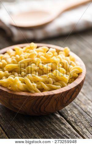 Uncooked gemelli pasta in wooden bowl.