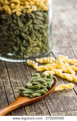 Uncooked spinach gemelli pasta in wooden spoon.