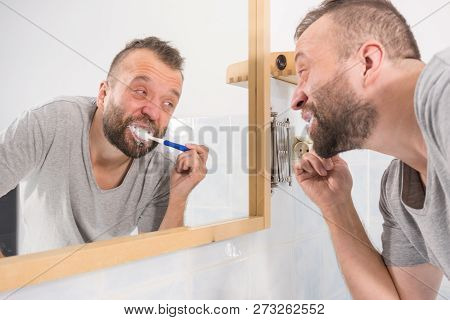 Adult Man Brushing His Teeth Looking At His Bathroom Mirror During Morning Hygiene Routine Being Bor