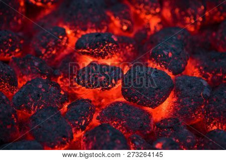 Coals smolder and glow. Residual flame from smoldering coals in cinder, closeup view. Flicker of burning coals at night.