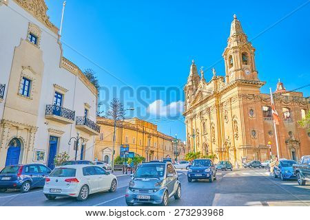 Naxxar, Malta - June 14, 2018: The Traffic In The Center Of The Town With A Huge Parish Church On Th