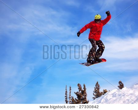 Snowboardista skoky vzduchem s tmavě modrou oblohou v pozadí