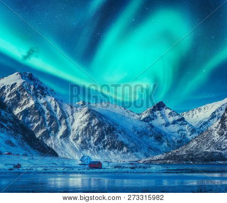 Northern Lights Above Snowy Mountains, Frozen Sea Coast And Houses In Lofoten Islands, Norway. Auror