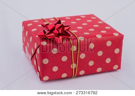 Red Gift Box On Gray Background. Present Box Wrapped In Dotted Craft Paper And Decorated With Satin 