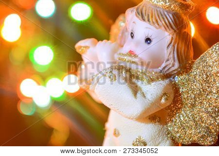 Figurine Of Little Angel With Golden Shiny Wings And Halo That Plays Flute On Shining Background Of 