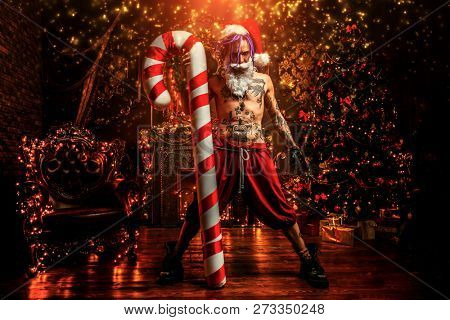Bad Santa concept. Portrait of a nude tattooed Santa with purple dreads demonstrating antisocial behavior, rudeness and aggression. 