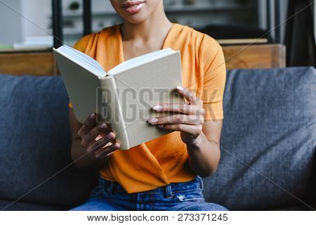 Cropped Image Of Mixed Race Girl In Orange Shirt Reading Book In Living Room