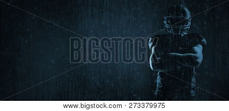 American football player standing with arms crossed against old weathered wall