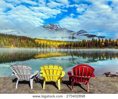 Rocky Mountains of Canada. Three comfortable multi-colored deck chairs stand by the Piramid lake.  Concept of ecological, active and photo-tourism