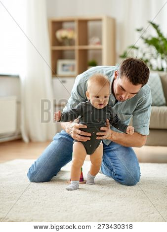 family, toddling and fatherhood concept - father helping little baby daughter with walking at home