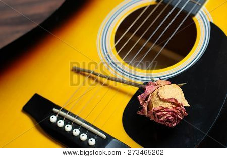 Acoustic Guitar With Dried Roses On The Wooden Table. Template For Advertising A Concert Of Memory S