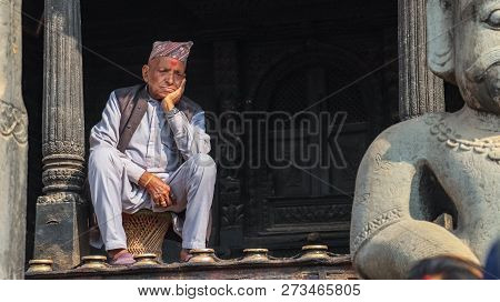 Bhaktapur, Nepal - December 8 2018: An Elderly Nepali Man Sitting Infront Of A Temple.