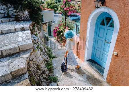 Travel Tourist Blonde Woman With Sun Hat Walking Through Narrow Streets Of An Old Greek Town To The 