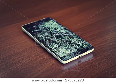Black Smartphone With Broken Screen On The Wooden Table. Phone Repair Concept. Old Broken Phone With