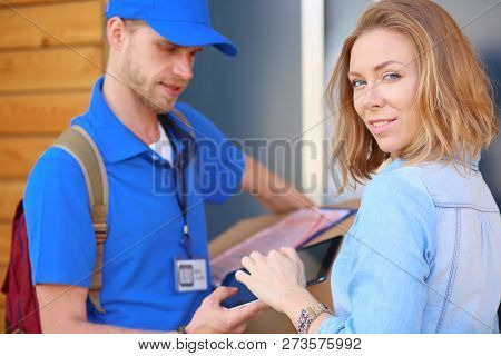 Smiling delivery man in blue uniform delivering parcel box to recipient - courier service concept. Smiling delivery man in blue uniform