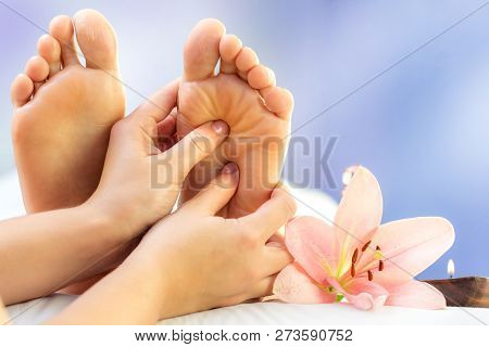 Macro Close Up Of Hands Massaging Female Foot. Feet Next To Flower And Candle Against Colourful Back