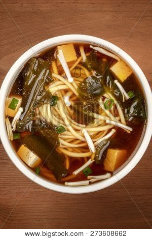 A Closeup Photo Of A Bowl Of Miso Soup With Tofu, Scallions, Noodles, Wakame Seaweed And Enoki Mushr
