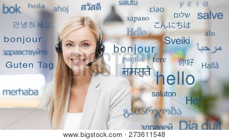 translation, business and technology concept - smiling female translator or operator in headset at office over greeting words in different foreign languages