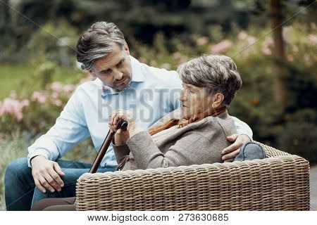 Sad Grey Senior Lady With Walking Cane Sitting In The Garden With Her Son