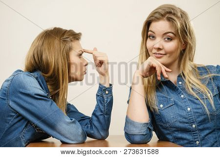 Woman Saying Bad Things About Her Over Confient Female Friend. Pointing At Forehead, Stupidity Gestu