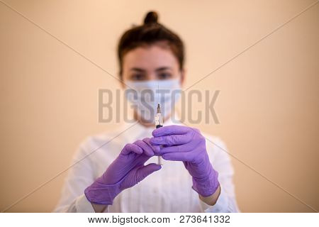 A Young Woman In A Medical Mask With A Syringe In Her Hands