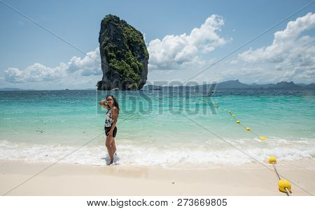 Woman Standing In Water At Edge Of Beach With Tropical Island In The Background