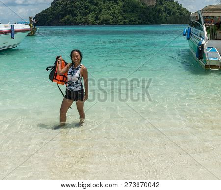Asian Woman Standing In Water On Tropical Island Holding Orange Life Jacket
