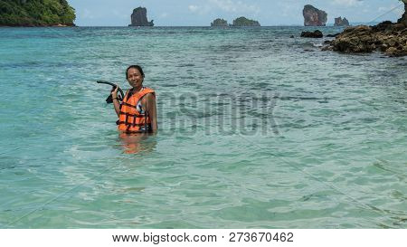 Woman Standing In Water In Orange Life Jacket Holding Mask And Snorkle