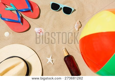 vacation and summer holidays concept - straw hat, flip flops, sunglasses, beach ball and sunscreen oil with seashells on sand