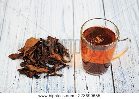 Cup Of Hot Black Tea And Dried Tea Leaves On Wooden Table