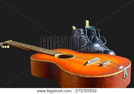Rock And Roll Concept. Black Boots And Acoustic Guitar. Rock And Roll Boots On Black Background.
