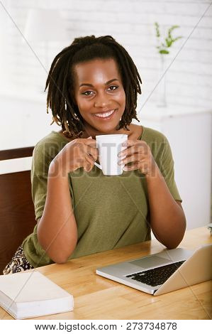 Happy Young Black Woman Sitting At Office Table And Drinking Big Cup Of Coffee