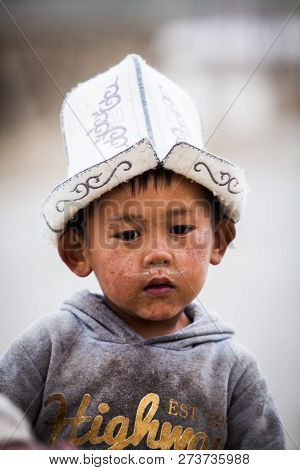 Murghab, Tajikistan - June 21, 2017: A Child Walks Down A Street, Wearing A Traditional Hat, In Murg