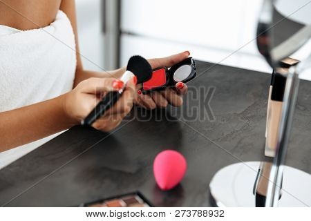 Close up of a woman wrapped in bath towel doing her makeup over a table with a mirror