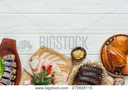 Top View Of Traditional Sliced Smoked Lard On Cutting Board, Rye Bread, Herring And Mini Pies On Whi