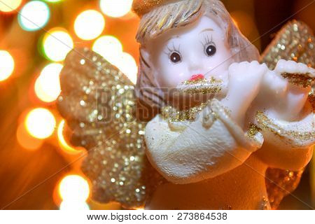 Figurine Of Little Angel With Golden Shiny Wings And Halo That Plays Flute On Shining Background Of 