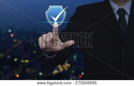 Businessman Pressing Security Shield With Check Mark Icon Over Blur Colorful Night Light City Tower 