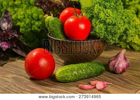 Tomatoes, Garlic Bulb And Cucumbers On A Wooden Table. Green Salad In The Background.