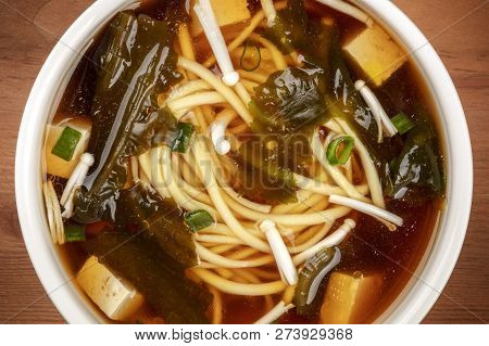 A Closeup Of Miso Shiru Soup With Tofu, Scallions, Noodles, Wakame Seaweed And Enoki Mushrooms