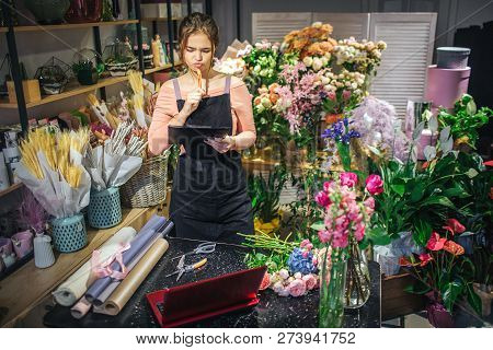Serious And Concentrated Young Florist Hold Black Planchette. She Think And Look At It. Floris Is Su