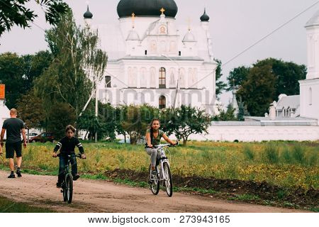 Mogilev, Belarus - August 18, 2018: Boy And A Girl Riding Bicycles Near The St. Nicholas Monastery C