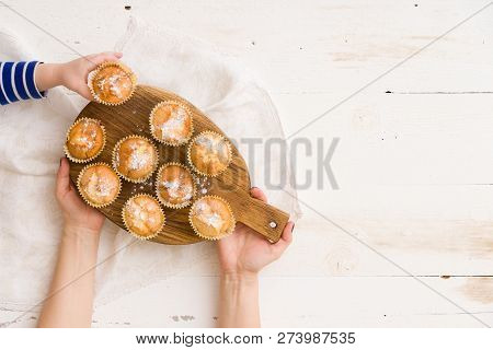 Top View On Womans Hands Holding Wooden Board With Homemade Muffins And Childs Hand Taking On Muffin