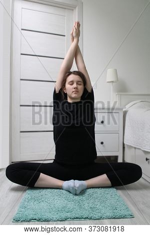 The Girl Is Sitting In The Lotus Position, Doing Yoga At Home. The Concept Of Yoga Classes As An Opp